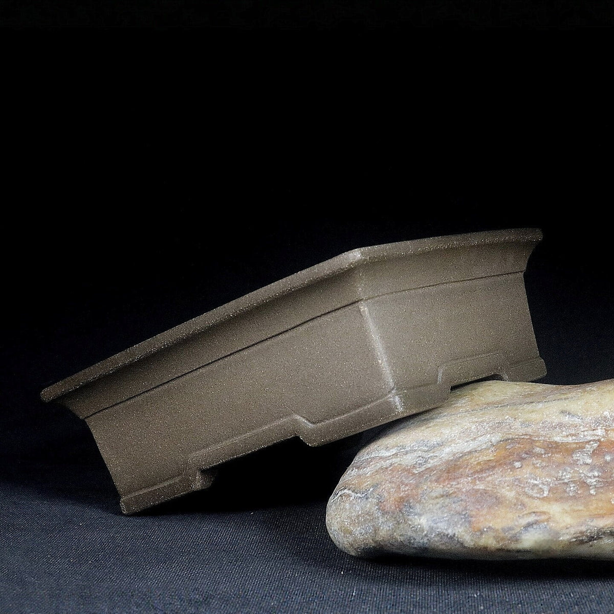 Gray rectangular bonsai pot tilted on a stone, showing side profile