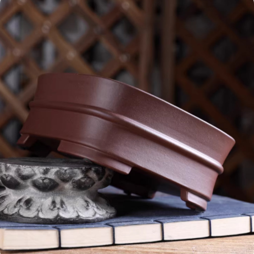 Brown rounded square pot tilted on a stone showing side and feet