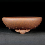 Speckled brown round pot with raised studs and curled decorative feet