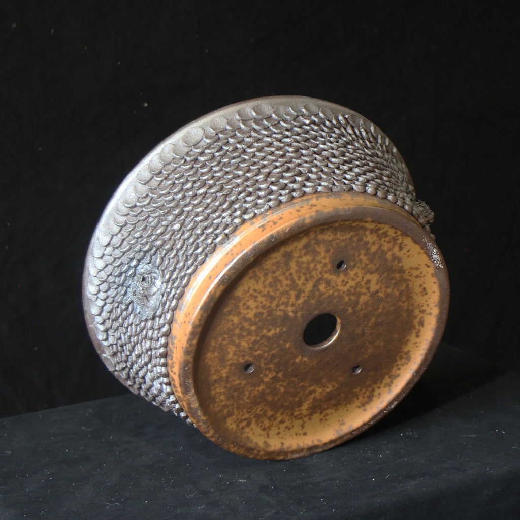 Underside of scale-textured bonsai pot showing central opening and smaller holes