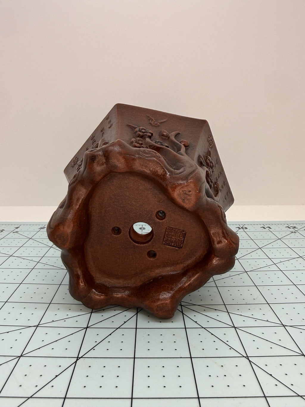 Tilted underside view of the hexagonal pot showing curled feet, drainage openings and an impressed seal