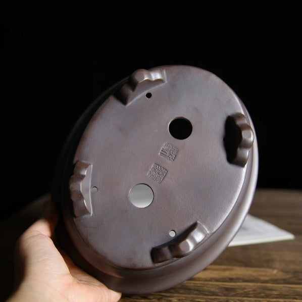 Hand-held underside view of the oval pot showing feet and impressed marks