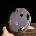 Hand-held underside view of the oval pot showing feet and impressed marks