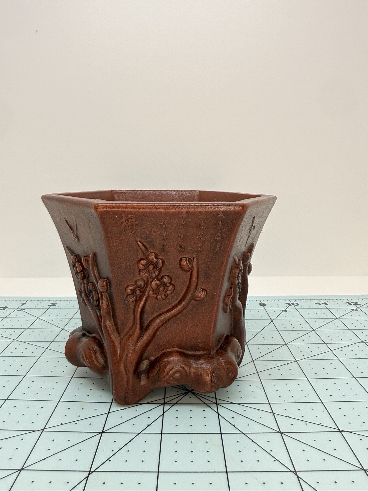 Hexagonal brown bonsai pot on a gridded mat, showing flared rim and raised branch decoration