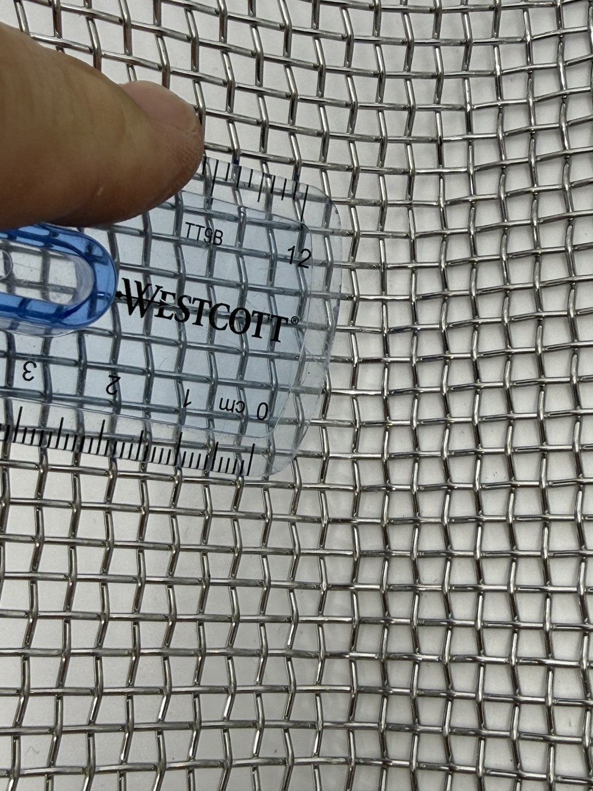Close-up of coarse square sieve mesh beside a ruler