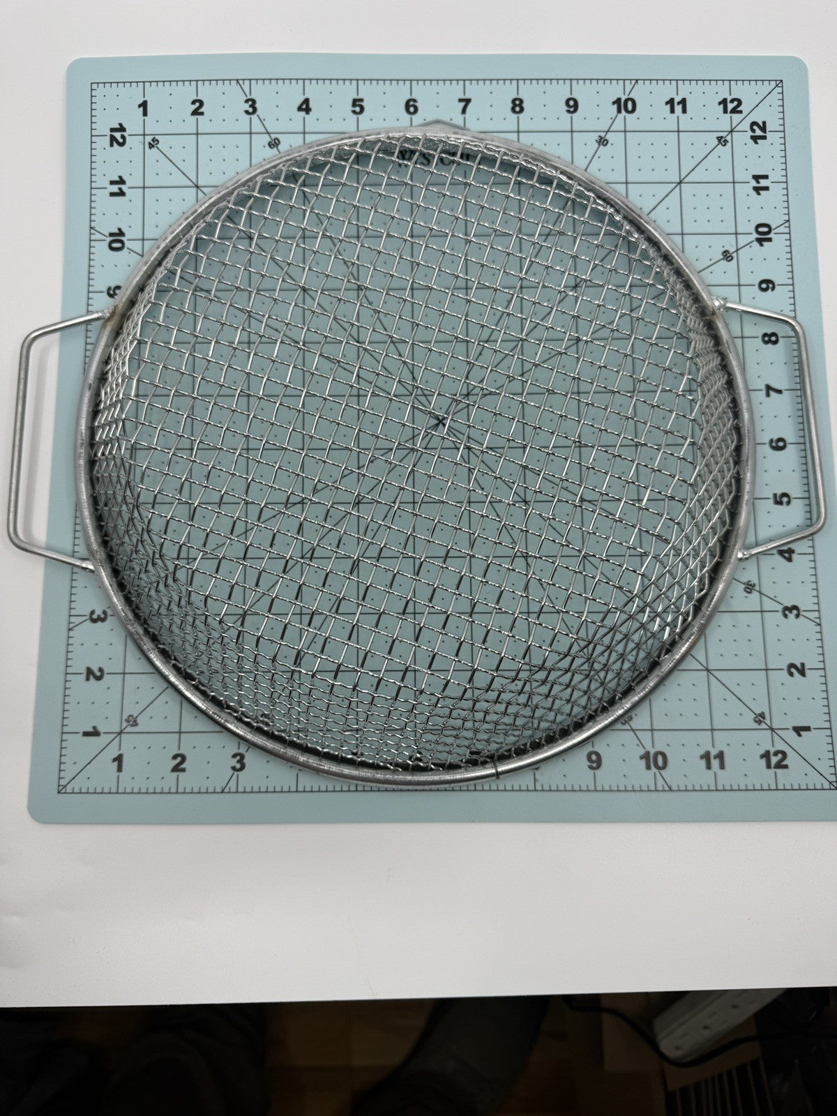 Overhead view of a round handled metal sieve on a measuring grid