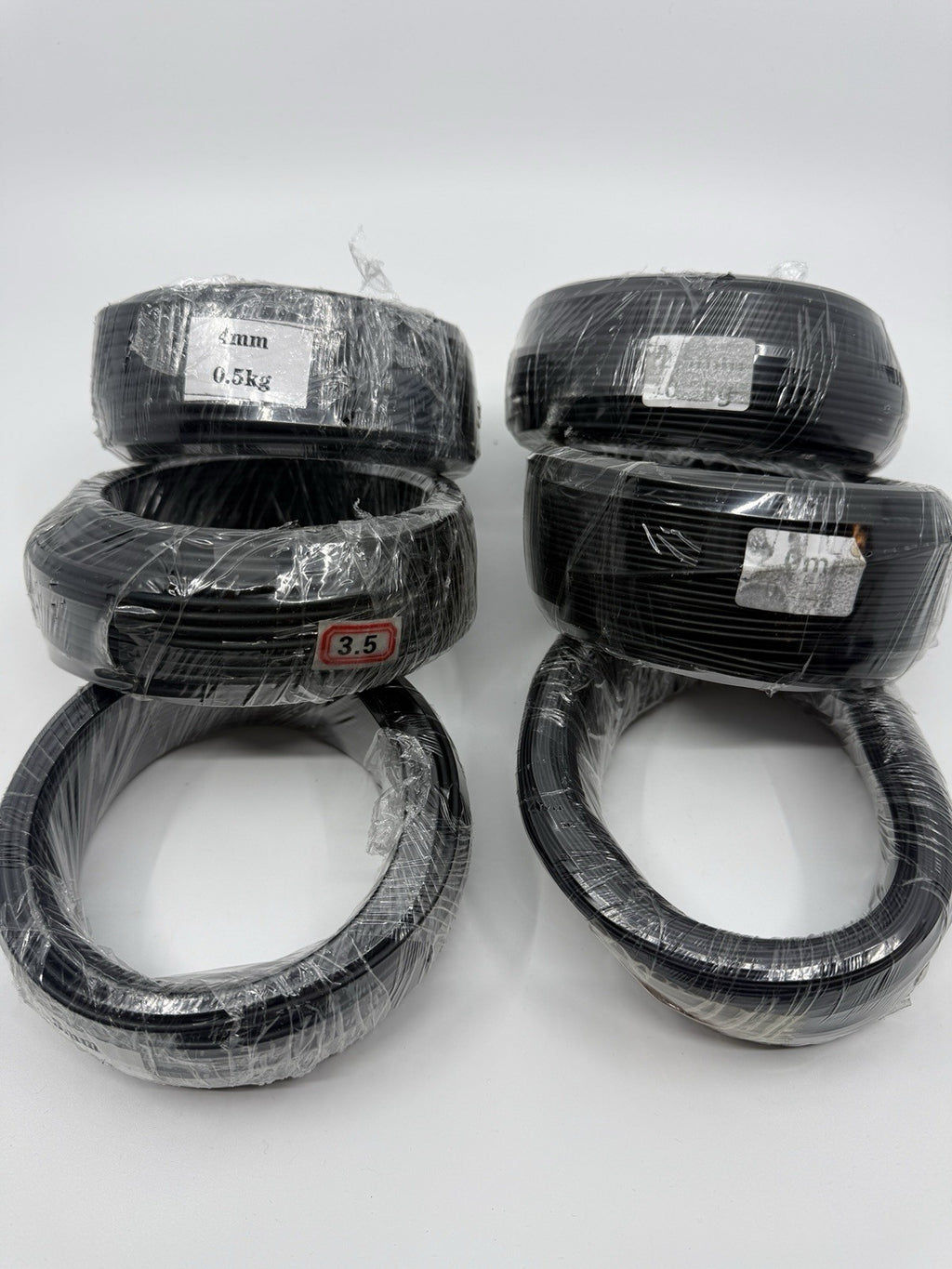 Six wrapped black wire coils arranged in two groups on a white surface