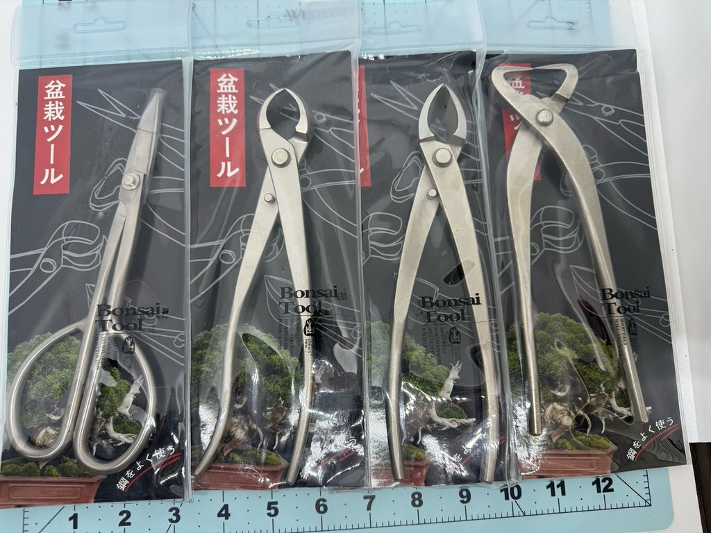 Four bonsai tools in individual clear packages laid side by side on a measuring mat