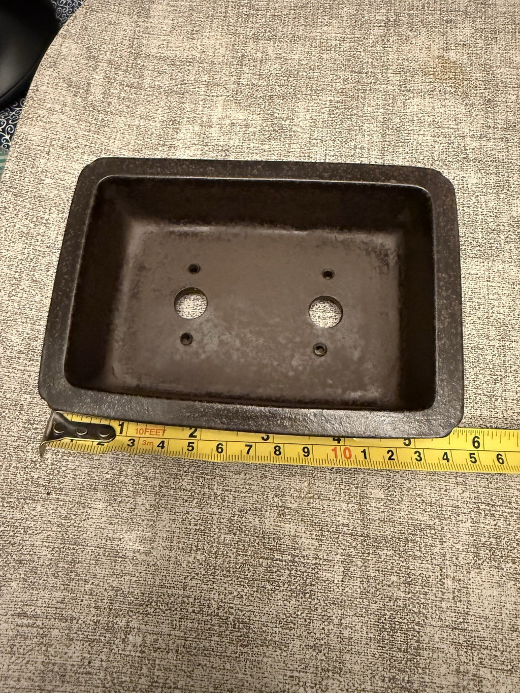 Dark rectangular pot photographed with a tape measure along its exterior length