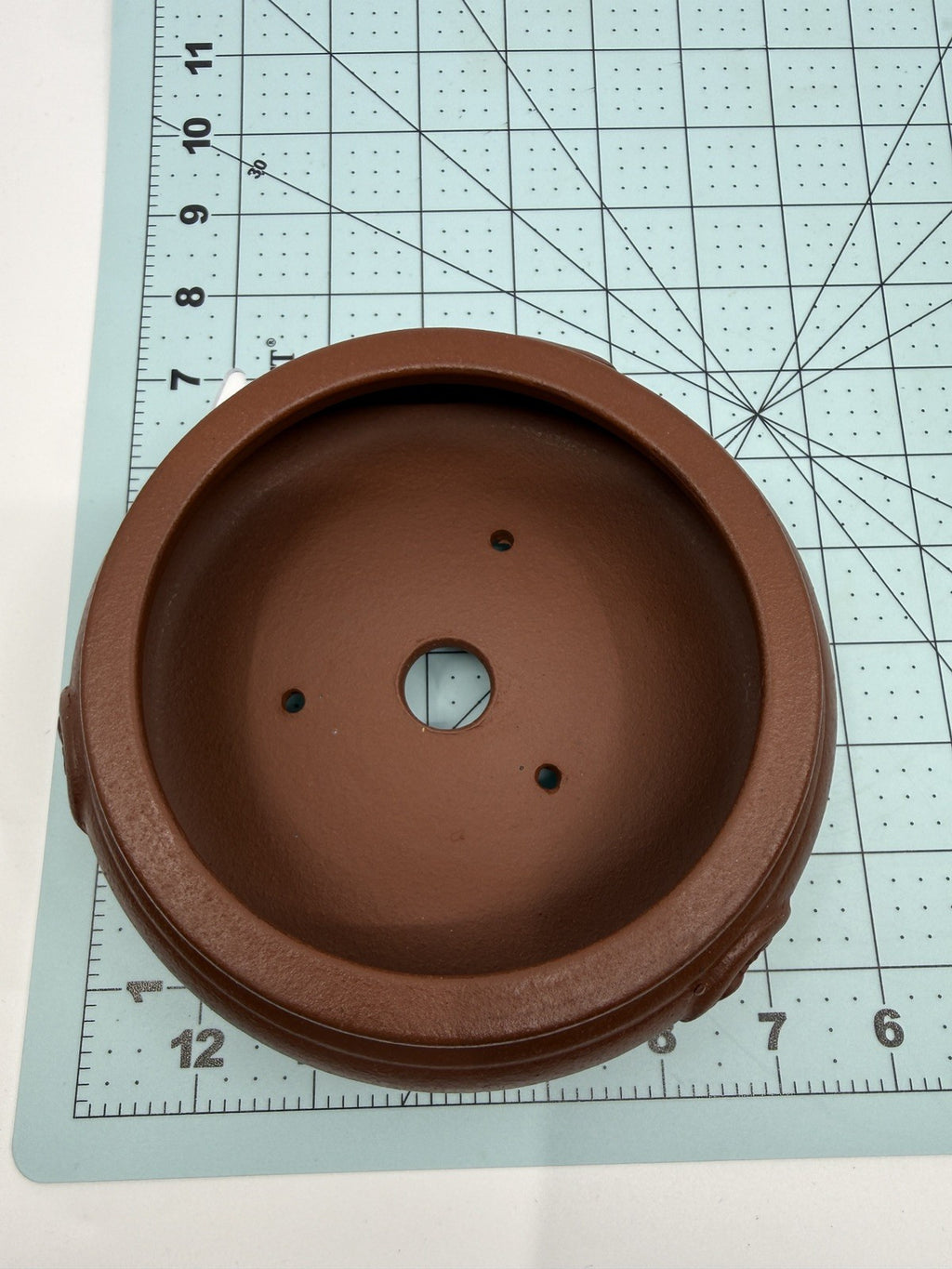 Overhead view of the brown pot's opening and drainage holes on a measuring grid