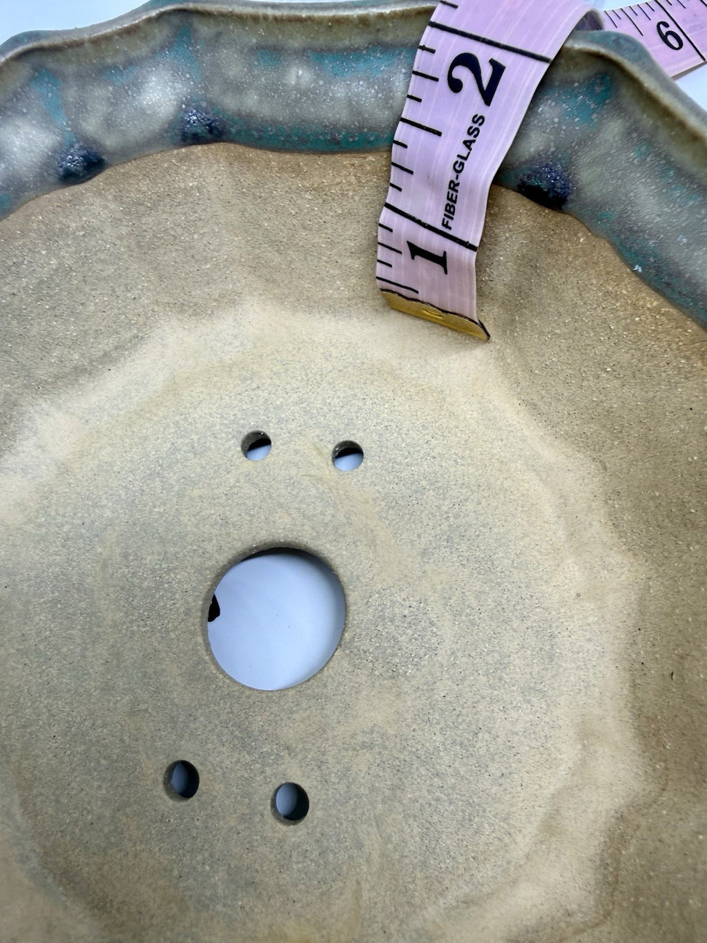 Tape measure inside the flower-shaped pot beside one large drainage hole and four smaller openings