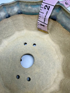 Tape measure inside the flower-shaped pot beside one large drainage hole and four smaller openings