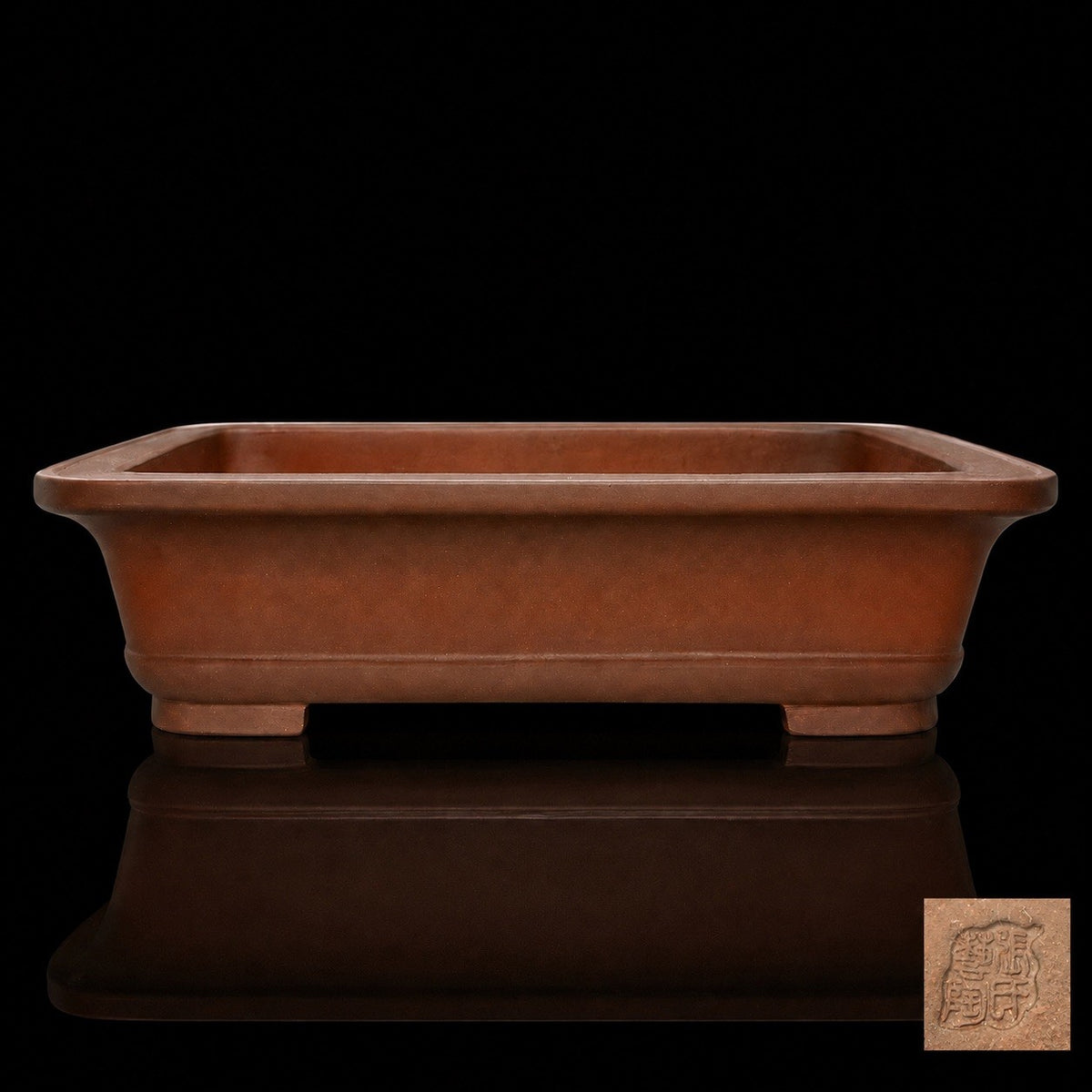 Brown rectangular pot on a reflective black surface with an inset of its impressed seal