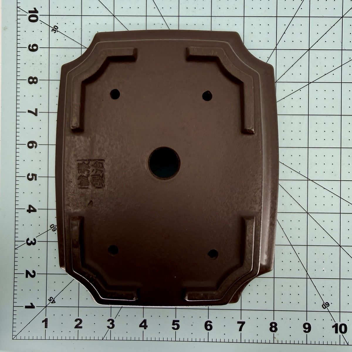 Base of the dark rectangular pot on a measuring mat, showing its seal and drainage holes