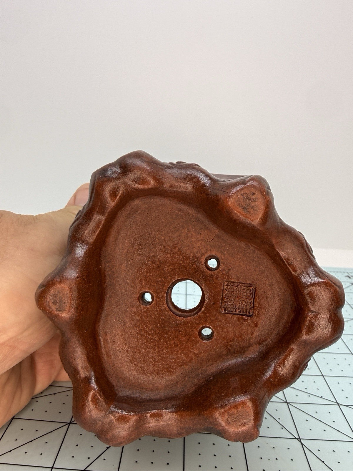 Hand-held close-up of the hexagonal pot's base with central drainage hole and three smaller openings