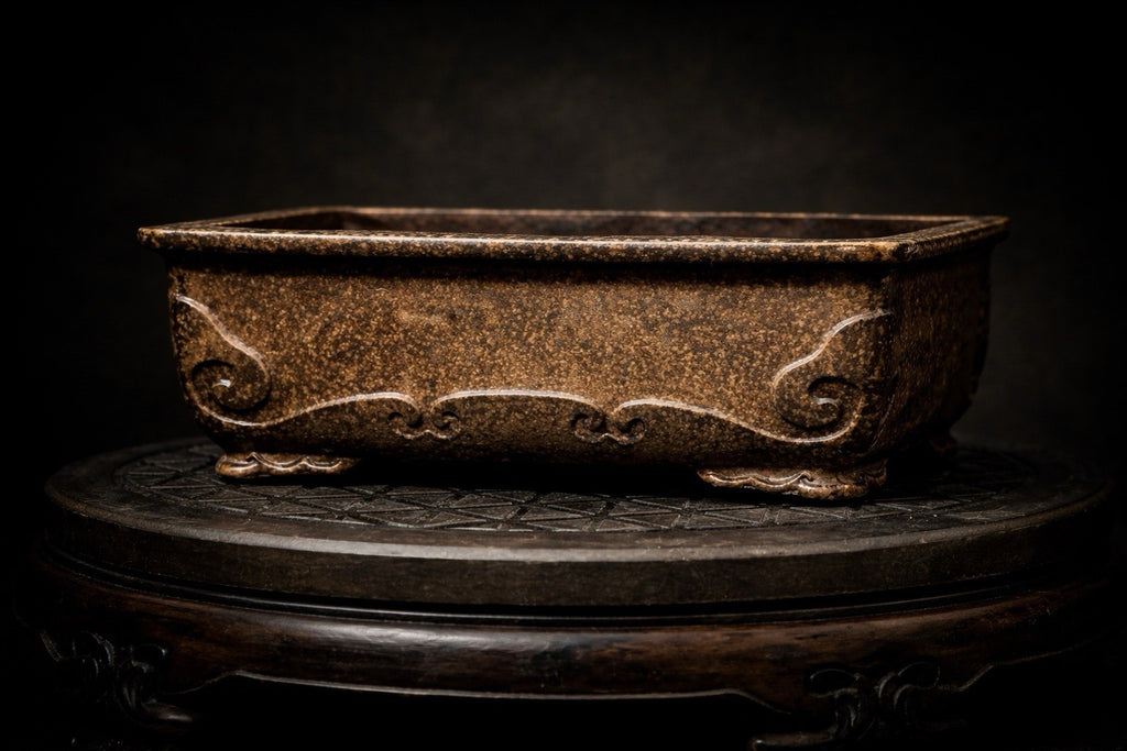 Dark brown rectangular pot with scrolling side relief displayed on a round wooden stand