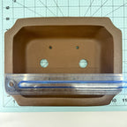 Ruler across the brown rectangular pot's interior opening on a gridded mat