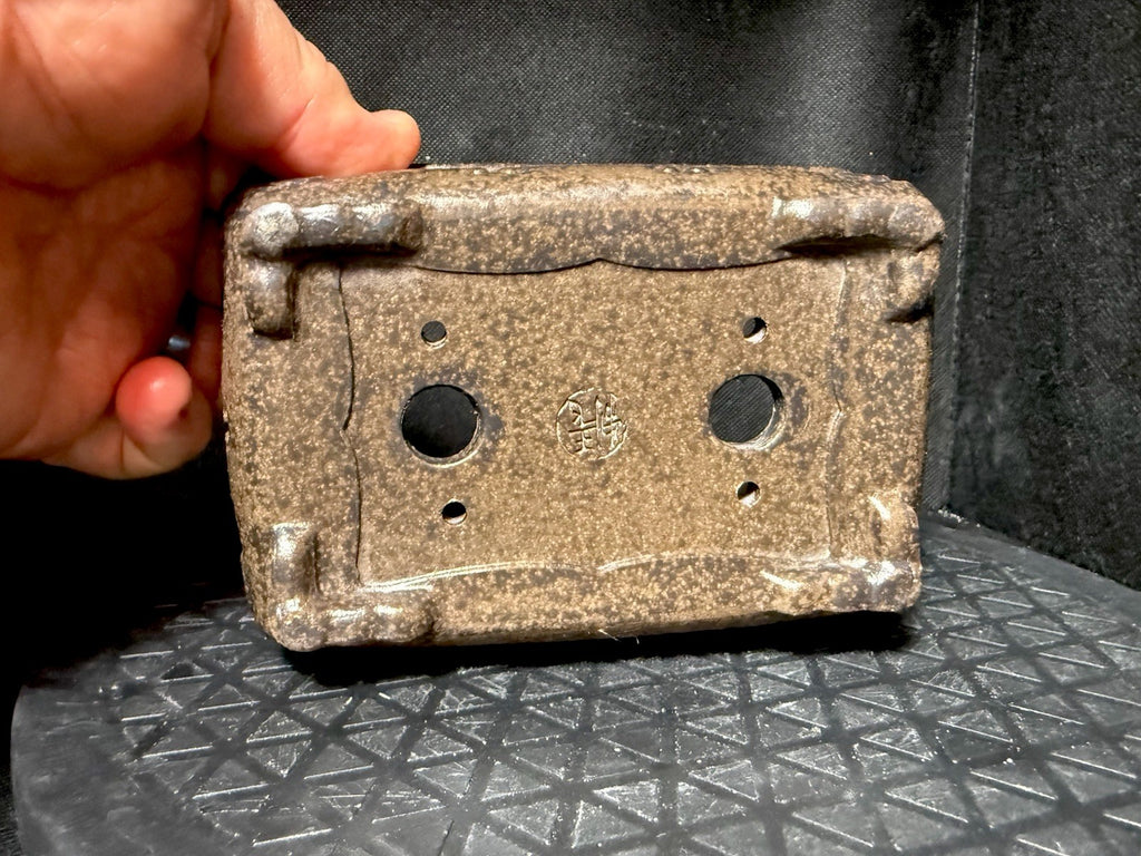 Hand-held underside view of the mottled pot showing drainage holes, corner feet and an impressed seal