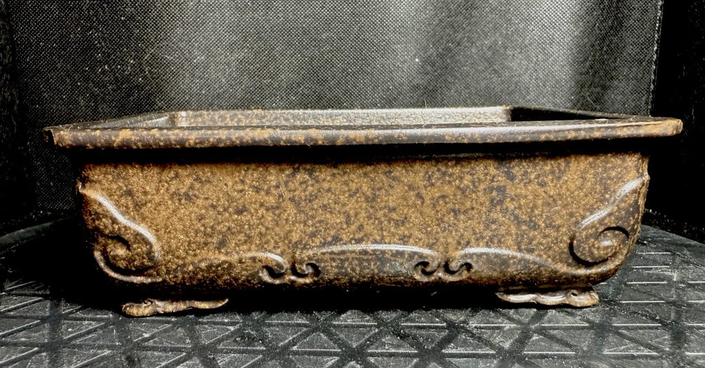 Front view of the mottled brown pot showing scrolling relief below its rim