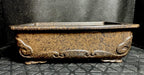 Front view of the mottled brown pot showing scrolling relief below its rim