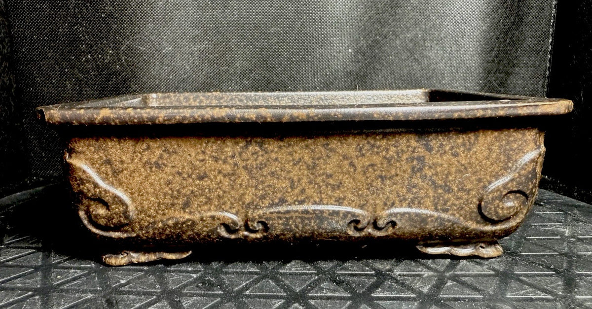 Front view of the mottled brown pot showing scrolling relief below its rim