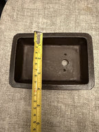 Tape measure spanning the width of a dark rectangular pot's opening