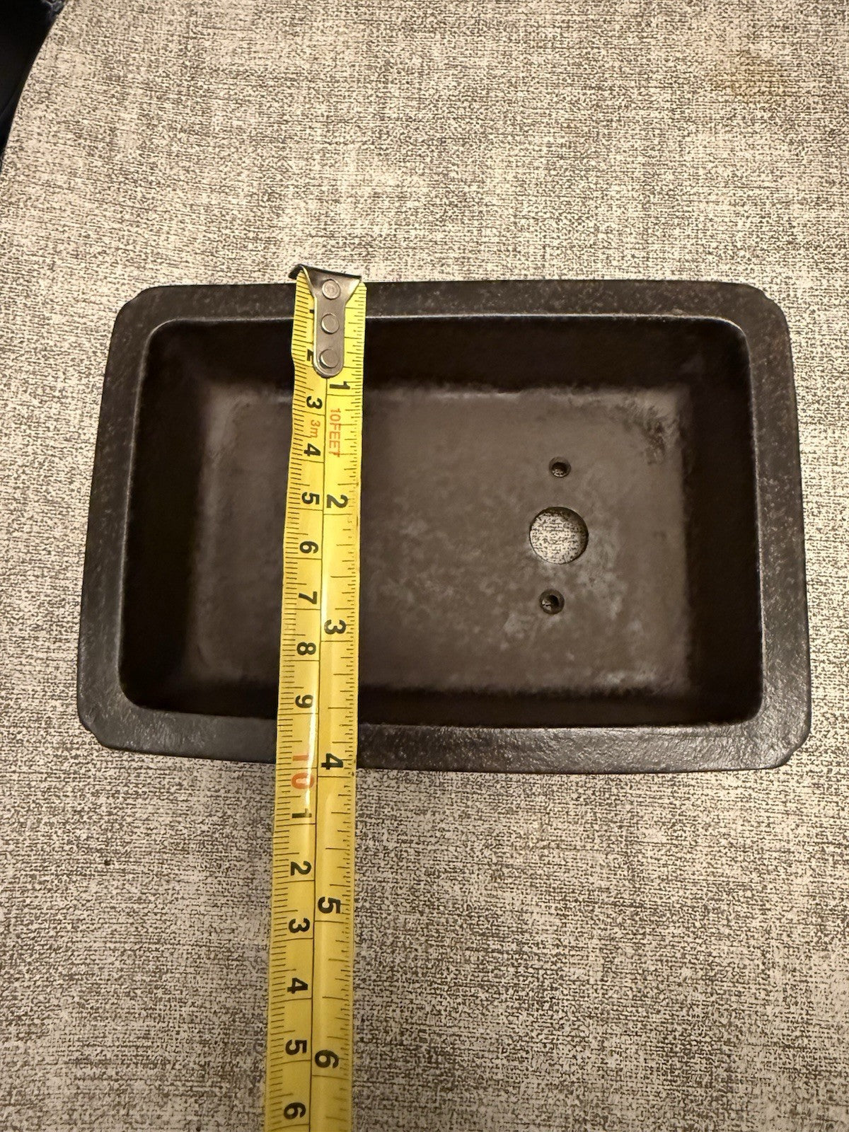 Tape measure spanning the width of a dark rectangular pot's opening