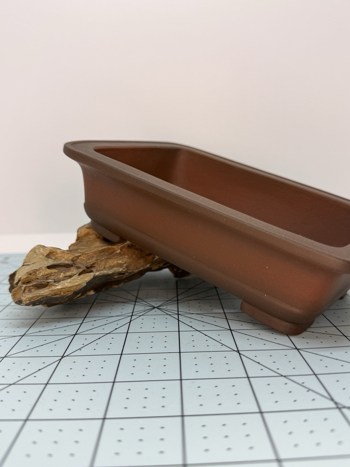 Brown rectangular pot tilted on a rock to show its side profile and rim