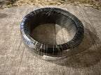 Overhead view of a dark wire coil wrapped in clear plastic on fabric
