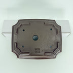 Underside of the dark rectangular pot showing corner feet, drainage openings and an impressed seal