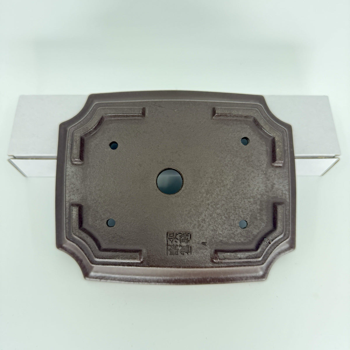 Underside of the dark rectangular pot showing corner feet, drainage openings and an impressed seal