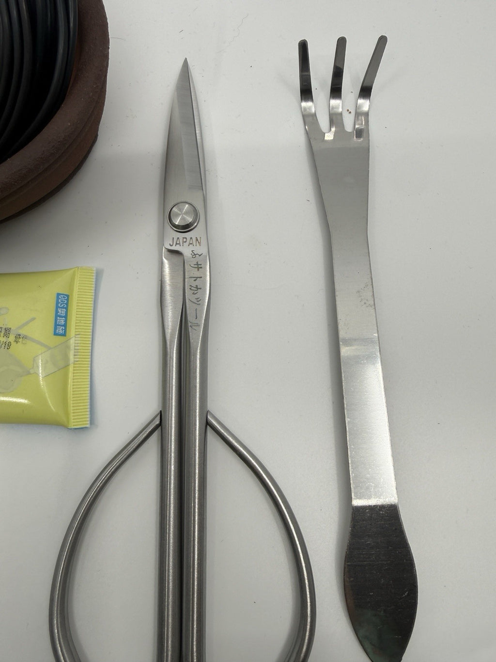 Close-up of silver bonsai scissors and a three-prong rake with flat spatula end