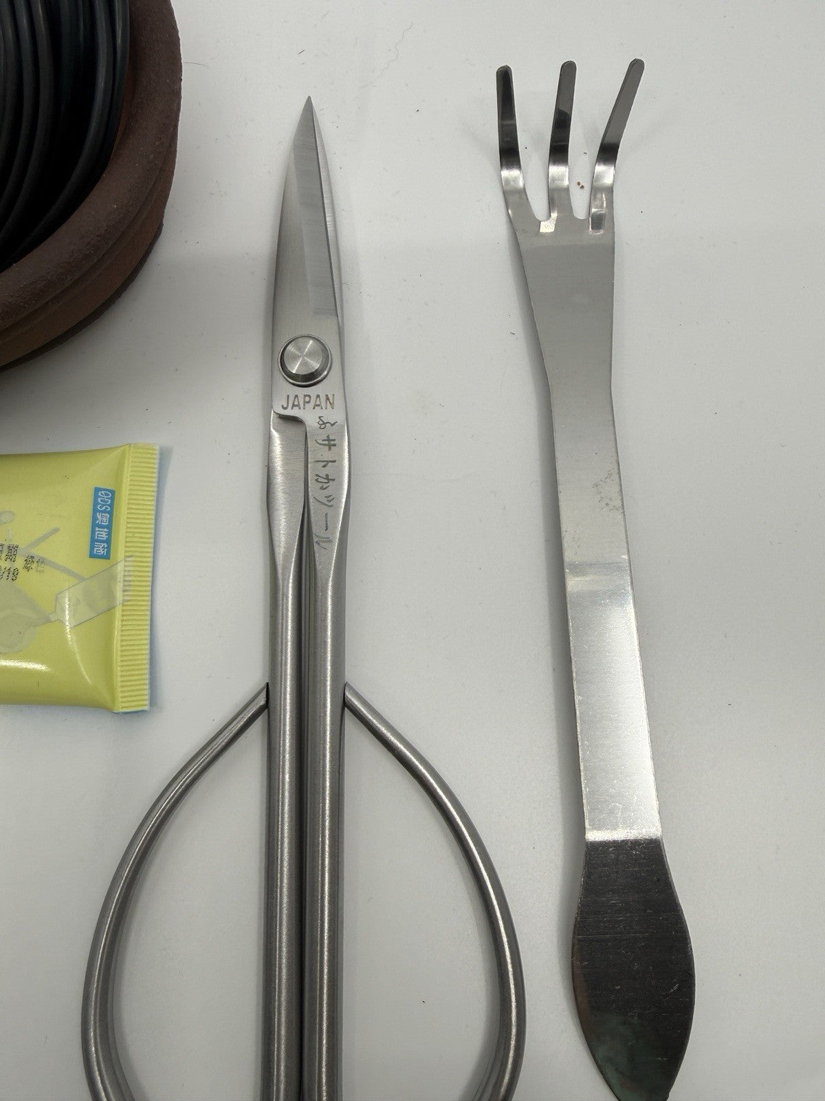 Close-up of silver bonsai scissors and a three-prong rake with flat spatula end