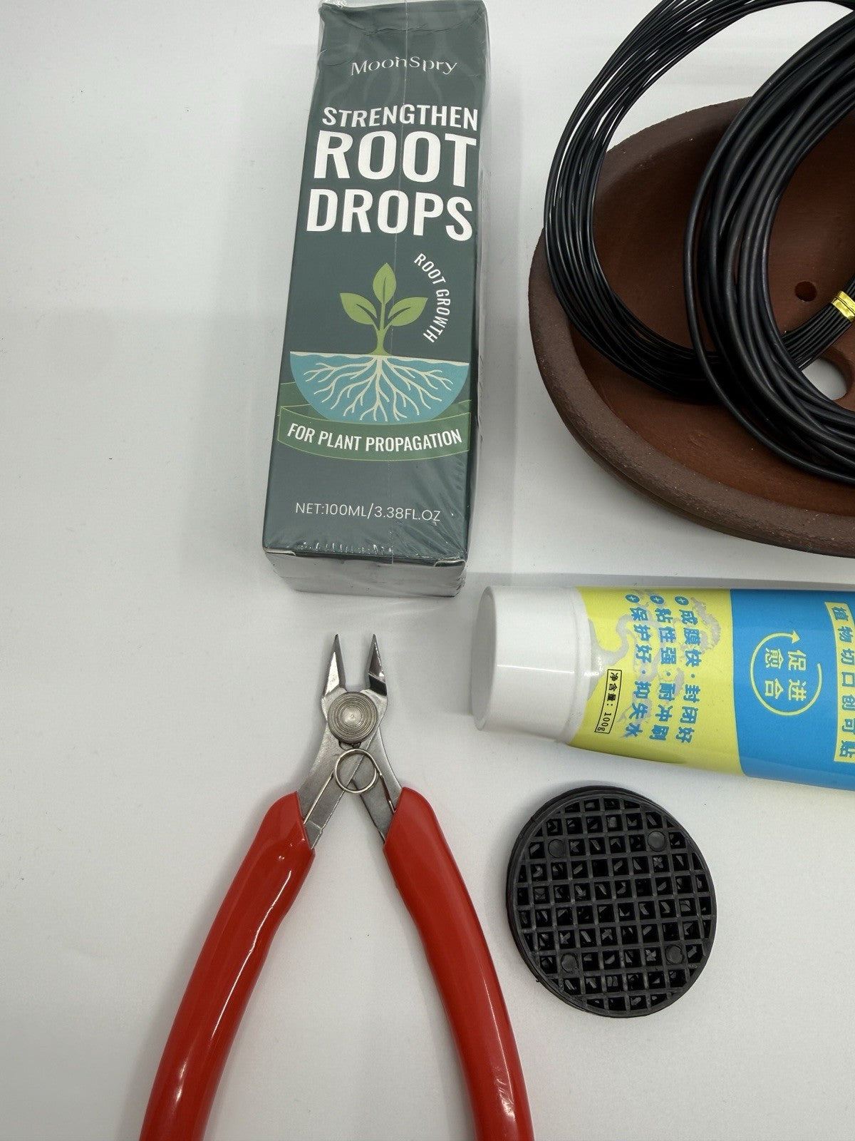 Close-up of Root Drops packaging, red-handled cutters, mesh disc and brown pot
