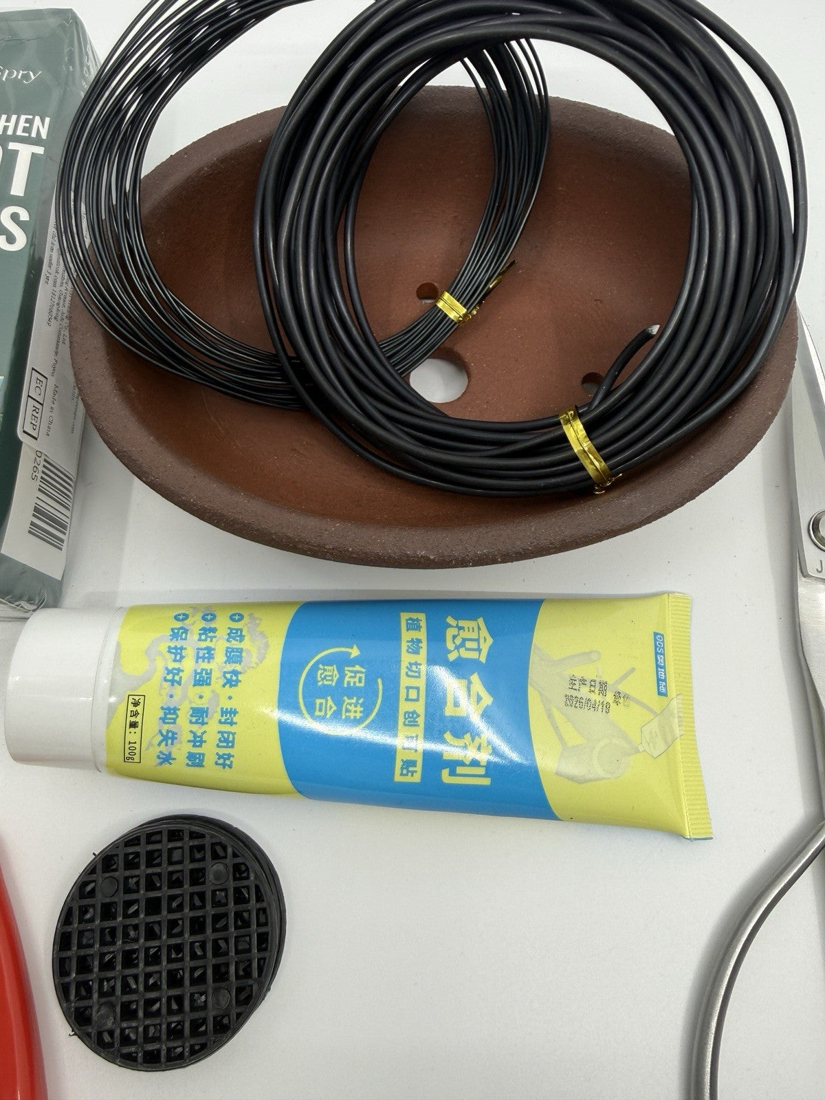 Wire coils resting in a brown oval pot beside a yellow-labeled tube and mesh disc