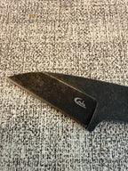 Close-up of the dark knife blade and its small white logo on textured fabric