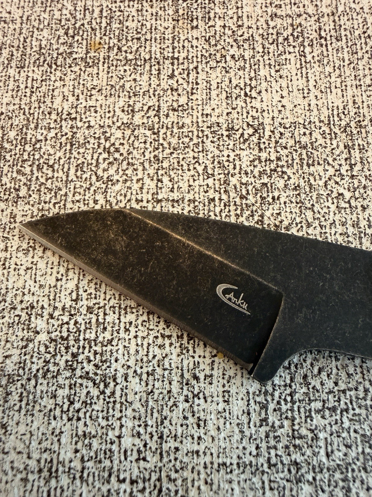 Close-up of the dark knife blade and its small white logo on textured fabric