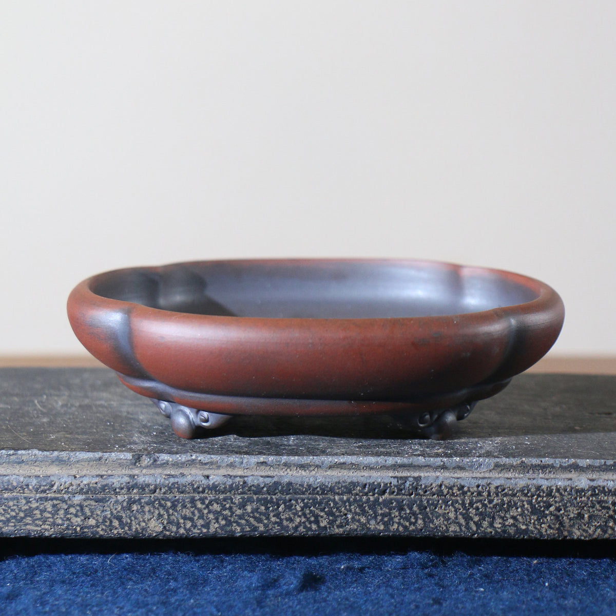 Side view of red-brown lobed bonsai pot on decorative feet