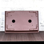 Underside of brown rectangular bonsai pot with corner feet and two large holes