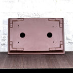 Underside of brown rectangular pot showing corner feet and openings