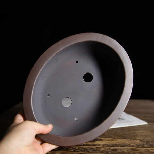 Hand holding the oval pot to show its interior and two drainage holes