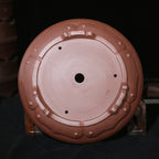 Underside of round brown pot showing central opening and decorative feet