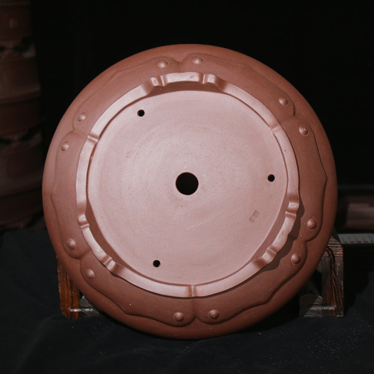 Underside of round brown pot showing central opening and decorative feet