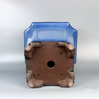 Underside of blue square pot showing central opening and four corner feet