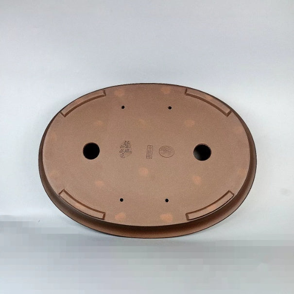Underside of brown oval pot showing two large openings, feet and stamped marks