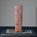 Slender reddish-brown pot with branch illustration on a stone stand