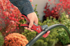 Hand using a red cutting tool on black irrigation tubing in a garden