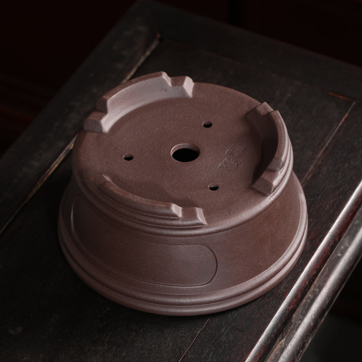 Underside of brown round pot showing central opening and small holes
