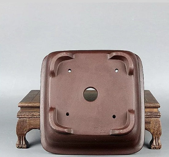 Underside of brown square pot showing large central opening and corner feet