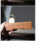 Hand holding the red-brown pot with calligraphy facing forward